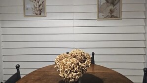 Ein Esstisch mit einem Blumenarrangement in der Mitte, begleitet von zwei gerahmten Pflanzenbildern an einer weißen Wand.