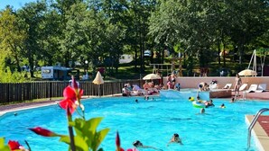 Ein Schwimmbecken mit Schwimmern und entspannenden Personen, umgeben von Bäumen und einem Zaun.
