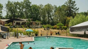 Ein Swimmingpool, umgeben von einem eingezäunten Bereich mit Liegestühlen und Sonnenschirmen.