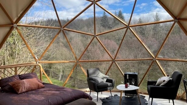 A geodesic dome interior with a bed, two chairs, a small table, and a view of a forest. - ZEcamping piscine chiens acceptés jacuzzi locatif BBQ 30m2 4 pers (Saint-Constant-Fournoulès)