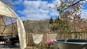 A wooden deck with a hot tub, a covered dining area, and a chair with a pink towel. - ZEcamping piscine chiens acceptés jacuzzi locatif BBQ 30m2 4 pers (Saint-Constant-Fournoulès)