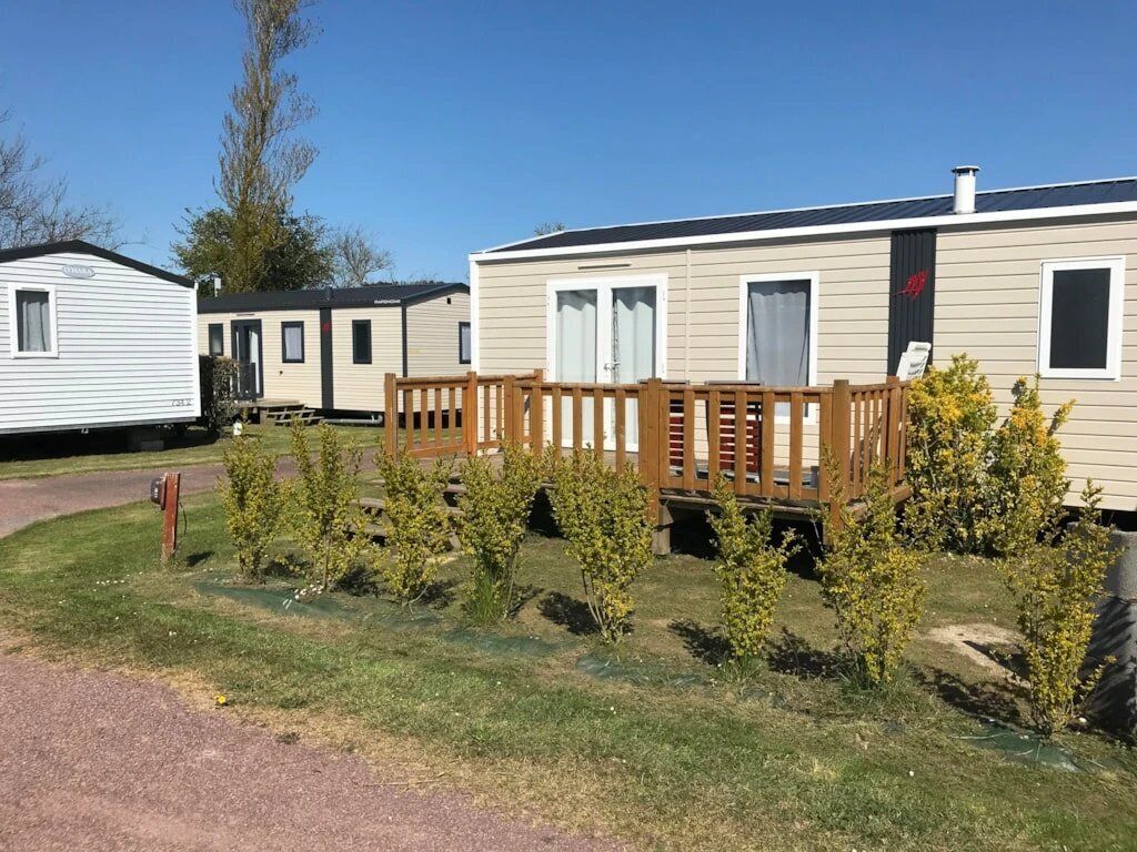 Ett husvagn med en träveranda och några små buskar framför.