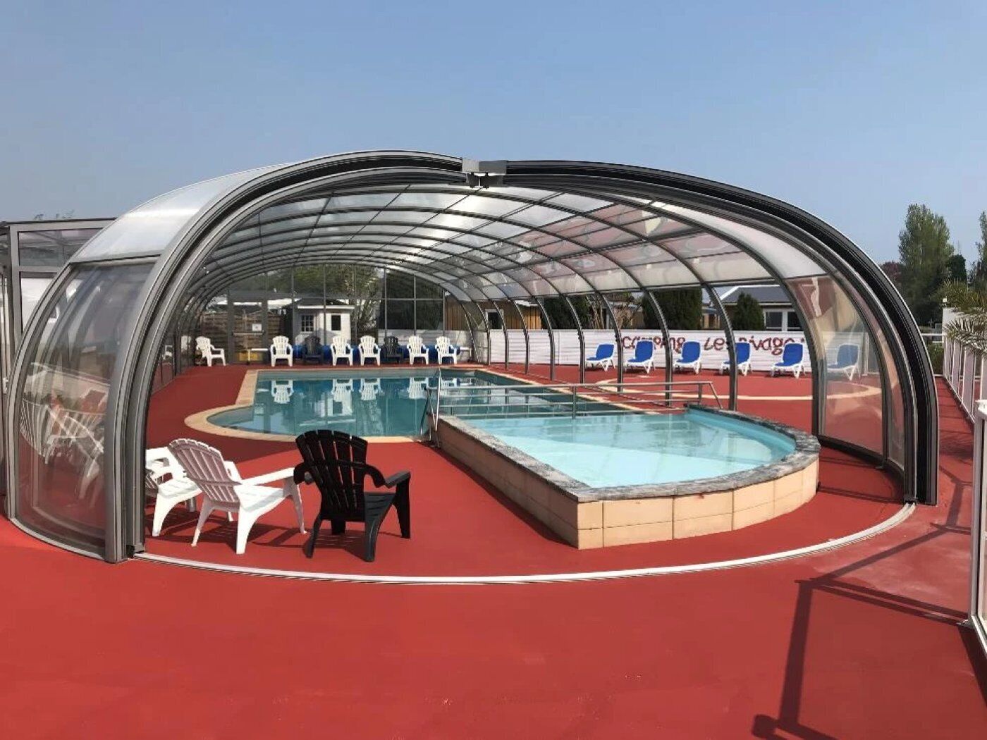 A covered swimming pool with a glass enclosure, red flooring, and several lounge chairs.