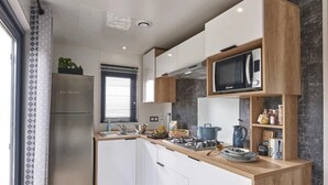 A compact kitchen with a microwave, stove, and sink. There is a window with blinds and a plant on the counter. - ZEcamping 4* familial 500m plage piscine couverte mobil-home TV LV BBQ (Morsalines)