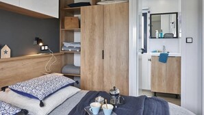 A bedroom with a bed, bedside tables, a wardrobe, and a bathroom with a sink and mirror. - ZEcamping 4* familial 500m plage piscine couverte mobil-home TV LV BBQ (Morsalines)