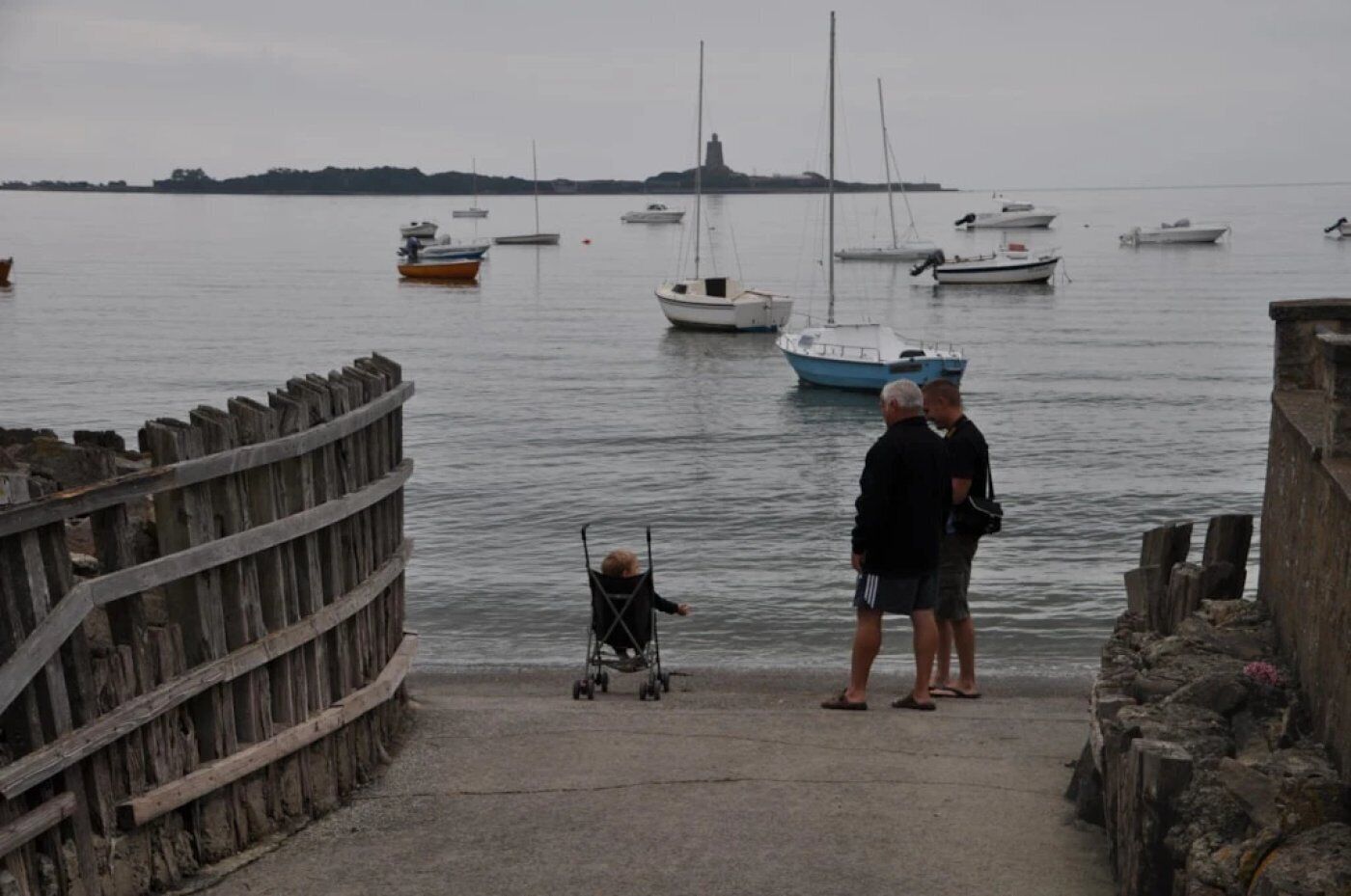 A pier with a wooden railing, a person in a wheelchair, and a man standing by the water.