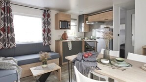 Un espacio habitable compacto con kitchenette, zona de comedor y área de estar con sofá y mesa.