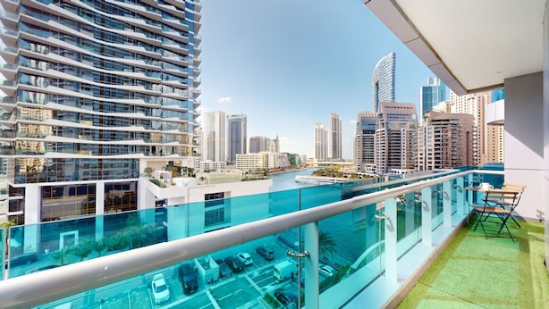 A high-rise building with a glass balcony overlooking a marina and cityscape.