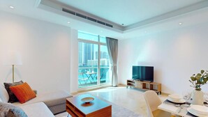 A modern hotel room with a large window, a flat-screen TV, a dining area, and a sofa.