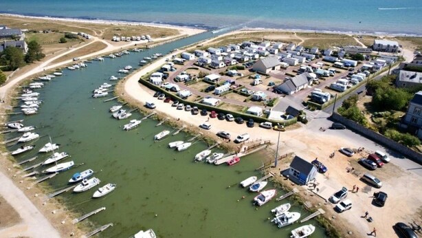 An aerial view of a marina with boats docked along the water's edge, surrounded by residential buildings and a sandy beach. - ZEcamping 3 étoiles restaurant et aire de jeux proche océan (Quinéville)