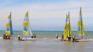 A beach with several sailboats and people preparing them. - ZEcamping 3 étoiles restaurant et aire de jeux proche océan (Quinéville)