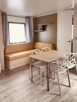 Una habitación pequeña con una mesa y sillas de madera, un banco acolchado y una ventana con cortinas.