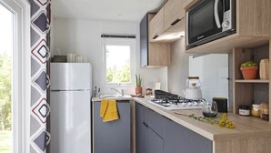 A compact kitchen with a refrigerator, stove, microwave, and a window. - ZEcamping 3 étoiles restaurant et aire de jeux proche océan (Quinéville)