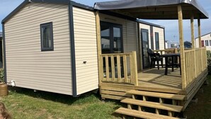 A mobile home with a deck and a covered patio area. - ZEcamping 3 étoiles restaurant et aire de jeux proche océan (Quinéville)