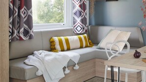 A cozy seating area with a cushioned bench, a striped pillow, and a white throw blanket. - ZEcamping 3 étoiles restaurant et aire de jeux proche océan (Quinéville)