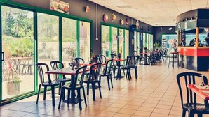 Un vaste espace de restauration intérieur, doté de grandes fenêtres, de chaises noires et de tables rouges.