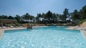 Une piscine à l’eau claire, entourée de chaises longues et de parasols, avec des arbres en arrière-plan.