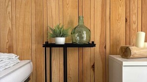 A bedroom with a wooden wall, a white bed, a small black metal side table with a potted plant and a green bottle, and a white dresser. - ZEcamping 4 étoiles locatif TV 32m2 (Saint-Hilaire-de-Riez)