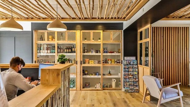 Ein modernes Interieur mit einem Holzbüro, Regalen mit unterschiedlichen Gegenständen und einer Sitzecke mit einem Sessel.