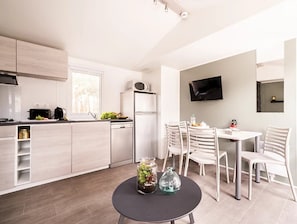 A modern kitchen with white cabinets, a built-in oven, and a dining area with a table and chairs. - ZEcamping 4* avec parc aquatique club enfant animations sauna hammam (Agde)