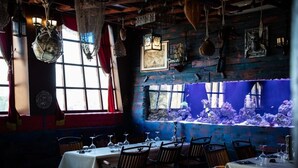 A restaurant with wooden walls, hanging decorations, and a large aquarium window.
