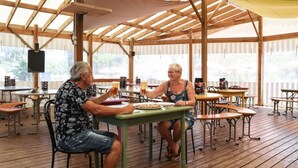 An outdoor dining area with wooden tables and chairs, covered by a wooden roof structure. - ZEcamping 3 étoiles chiens acceptés salle fitness piscine couverte (Saint-Julien-des-Landes)