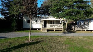 A white mobile home with a porch and a small tree in front. - ZEcamping 3 étoiles chiens acceptés salle fitness piscine couverte (Saint-Julien-des-Landes)