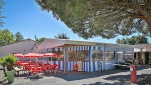 A small, striped building with a sign reading "Bienvenue au Camping le Paulcon". Outside, there are red chairs and umbrellas under a tree. - ZEcamping 3 étoiles chiens acceptés salle fitness piscine couverte (Saint-Julien-des-Landes)