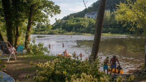 Ein Campingplatz am Seeufer mit Bäumen, einem Zelt und Menschen, die sich an Wassersportaktivitäten beteiligen.