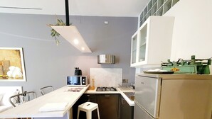 Une cuisine compacte avec un plan de travail blanc, une cuisinière à gaz, un réfrigérateur en acier inoxydable et une plante suspendue.
