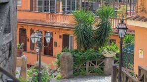 Une rue pavée menant à des immeubles à étages dotés de balcons, un mur de pierre et un portail en métal.