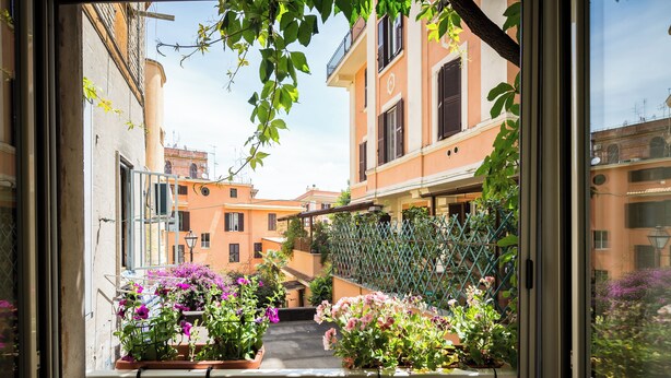 Une ruelle étroite bordée de bâtiments des deux côtés, un balcon orné de plantes en pot et une vue sur la rue.