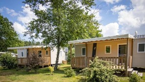 Une rangée de maisons mobiles dotées de terrasses et de fenêtres en bois, entourées d’herbe et d’arbres.