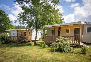 Une rangée de maisons mobiles dotées de terrasses et de fenêtres en bois, entourées d’herbe et d’arbres.