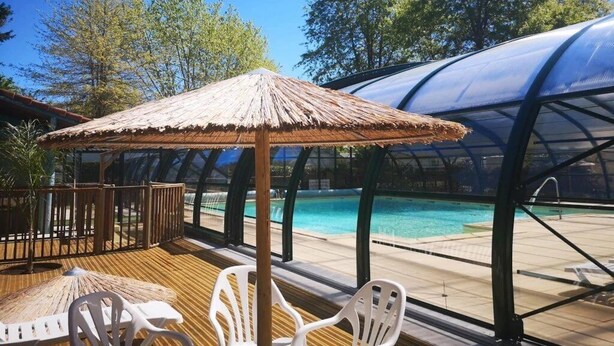 A poolside area with a thatched umbrella, white plastic chairs, and a transparent pool enclosure. - Cabane 4 étoiles - Piscine  - ccabhid (Azur)