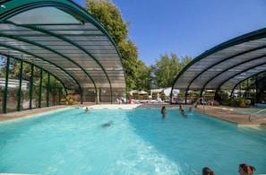 Une piscine dotée d’une structure de toit incurvée, entourée d’arbres et surplombée par un ciel dégagé.