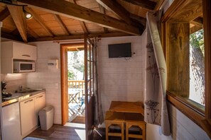 Une cuisine compacte équipée d’un four à micro-ondes, d’un évier et de placards en bois. On y trouve une petite table et un téléviseur fixé au mur.