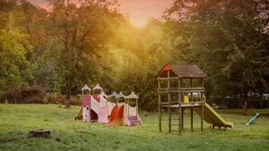A playground with a slide and climbing structures in a grassy field with trees in the background.
