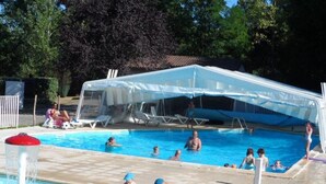 A swimming pool area with a covered seating area, lounge chairs, and a water play area for children.