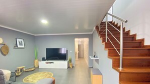 A modern living room with a flat-screen TV, a sofa, a coffee table, and a staircase. - Sea Breeze (São Roque)