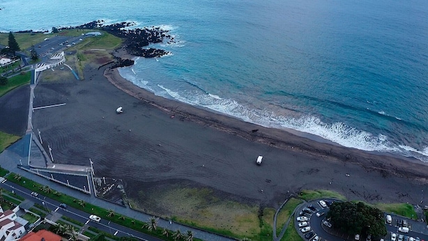 An aerial view of a coastal area with a beach, parking lots, and a road. - Sea Breeze (São Roque)