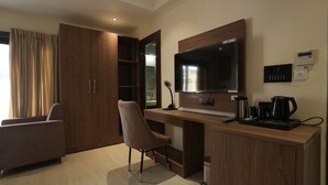 Une chambre d’hôtel moderne équipée d’un bureau en bois, d’un téléviseur à écran plat, d’une chaise, d’une armoire et d’une machine à café.