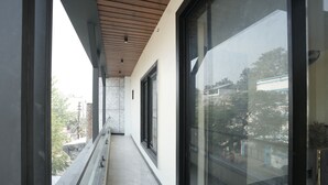 Un balcon étroit doté d’un plafond en bois, de grandes portes vitrées et offrant une vue sur les bâtiments et les arbres.