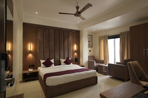 A modern hotel room with a large bed, a desk, a chair, and a ceiling fan. - Hotel SS4 Crystals (Lucknow)
