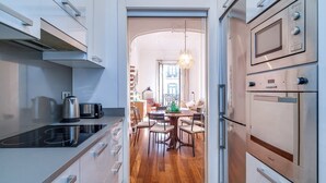 A modern kitchen with a built-in stove, a kettle, and a microwave. There is a dining area with a table and chairs visible through an open door.