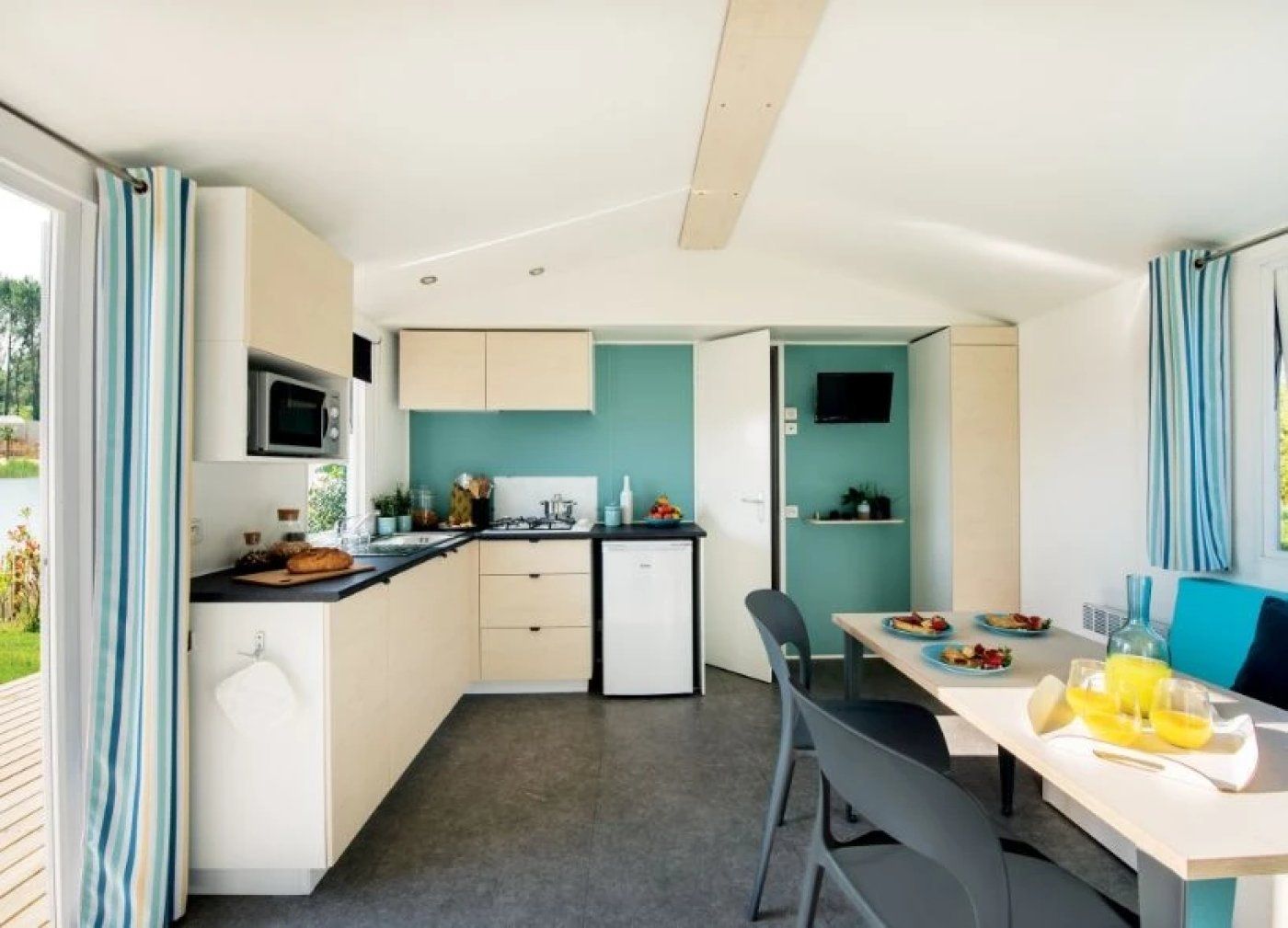 A compact kitchen with a microwave, stove, and sink, a dining area with a table and chairs, and a TV mounted on the wall.