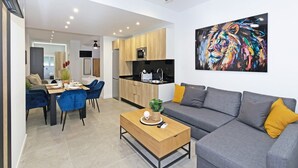 A modern living room with a grey sofa, a wooden coffee table, and a dining area with blue chairs.