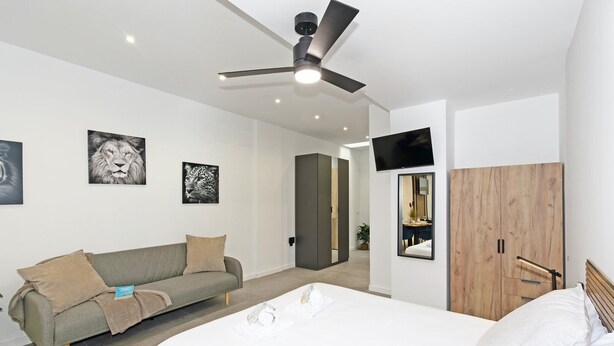 A modern bedroom with a bed, a sofa, a ceiling fan, and artwork on the walls.
