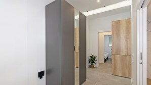 A modern hallway with a sliding door, a potted plant, and a glimpse of a bedroom with a bed and a nightstand.