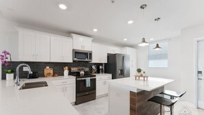 A modern kitchen with white cabinets, stainless steel appliances, and a central island with bar stools. - 3120-105 Resort Pool View Disney Universal Orlando (Kissimmee)